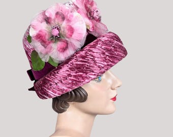 May include: A pink velvet hat with a large pink flower on top. The hat is trimmed with a black velvet ribbon.