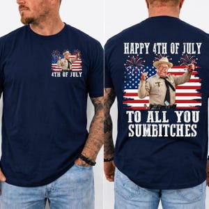 May include: A navy blue t-shirt featuring a graphic of a man in a sheriff uniform and cowboy hat against an American flag background with fireworks. The front has a small chest print, and the back displays the text HAPPY 4TH OF JULY TO ALL YOU SUMBITCHES.