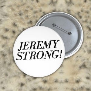 Peut inclure: Un badge rond avec une face blanche portant le texte noir JEREMY STRONG! écrit dans une police à empattement. Le dos du badge est en métal argenté et comprend un mécanisme d'épingle horizontal pour le fixer aux vêtements ou aux tissus.
