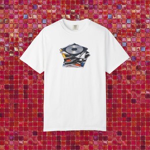 May include: A white short-sleeve t-shirt featuring a centered graphic print of a stack of multicolored compact discs. The design shows several stacked CD cases with visible metallic discs and colorful spines, displayed on a plain white fabric background.