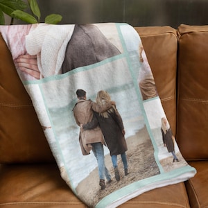 Op de afbeelding: Een zachte, witte fleece deken met een collage van foto's erop gedrukt. De foto's laten een stel zien dat over het strand loopt, een close-up van een hand die een trui vasthoudt en een vrouw die over het strand loopt.
