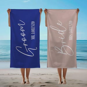 May include: Two beach towels, one blue with "Groom" and "MR. LORENZO" in white script, the other beige with "Bride" and "MRS. LORENZO" in white script.