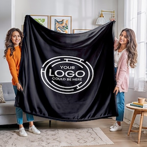 May include: Two people are holding a black fleece blanket with a white circle design that says "Your Logo Could Be Here".