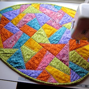 Pode incluir: Um corredor de mesa de patchwork colorido com um design geométrico em tons de verde, laranja, rosa, amarelo e azul. O corredor é oval e tem uma borda verde.