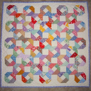 May include: A colorful patchwork quilt with a white background and a geometric pattern of squares and triangles. The quilt is made from a variety of fabrics in shades of pink, blue, green, yellow, and red.
