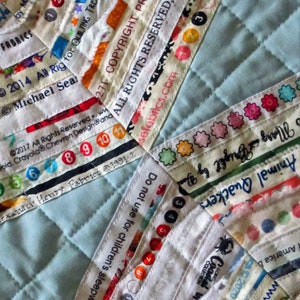 May include: A close-up of a blue quilted fabric with various white fabric strips sewn on top. The strips have different text printed on them, including "2014 All Rights Reserved", "Copyright Protected", "All Rights Reserved", and "Do not use for children's sleepwear".