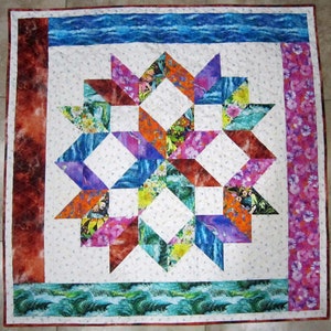 May include: A colorful quilt with a starburst pattern in the center. The quilt is made of various fabrics with floral and wave designs. The quilt is bordered with a red, blue, and pink fabric.