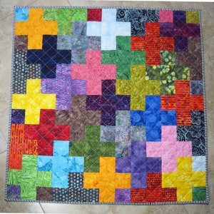May include: A colorful quilt made of fabric squares sewn together in a plus sign pattern. The quilt is made up of a variety of colors, including red, blue, green, yellow, purple, and brown. The quilt is quilted with a diamond pattern.