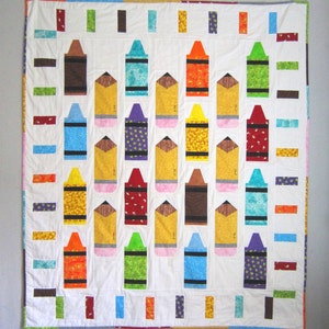 May include: A white quilt with a pattern of colorful crayons. The crayons are arranged in rows and columns, and each crayon is a different color. The quilt is made of fabric squares that are sewn together.
