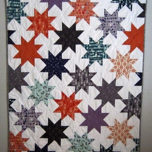 May include: A quilt with a white background and a pattern of stars in various colors, including orange, purple, teal, and black.