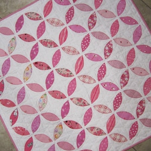 May include: A pink and white quilt with a repeating pattern of overlapping circles. The quilt is made of various pink fabrics with different patterns, including polka dots, stripes, and floral prints.