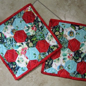 May include: Two red and blue quilted pot holders with a wintery floral pattern. The pot holders have a red border and are quilted with a diamond pattern.