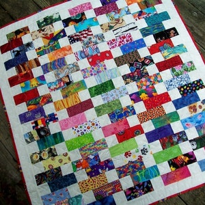 May include: A colorful patchwork quilt with a white background and a red border. The quilt is made up of many different fabric scraps, each with a unique pattern. The quilt is a great example of a scrappy quilt, which is a type of quilt that uses leftover fabric scraps.