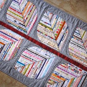 Pode incluir: Um corredor de mesa cinza com uma faixa vermelha e marrom no centro. O corredor é decorado com cinco grandes remendos em forma de folha feitos de retalhos de tecido coloridos. Os retalhos de tecido estão dispostos em um padrão listrado.