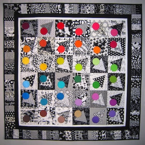 May include: A black and white quilt with a central square featuring a grid of colourful circles. The circles are arranged in a rainbow pattern, with red, orange, yellow, green, blue, indigo, and violet circles. The quilt is surrounded by a black border.