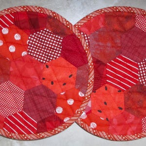 May include: Two red and white quilted pot holders with a patchwork design. Each pot holder is made of different red and white fabrics with a variety of patterns.