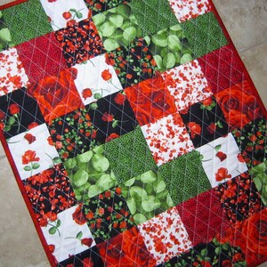 May include: A red, green, black, and white patchwork quilt with a floral pattern. The quilt is made of squares of fabric sewn together. The quilt is quilted with a diamond pattern.