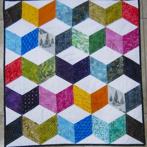 May include: A colorful quilt with a geometric design of 3D cubes. The cubes are made of various patterned fabrics in shades of blue, green, yellow, orange, purple, and pink, set against a white background. The quilt is bordered with a dark blue fabric.