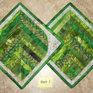 May include: Two green and white quilted placemats with a leaf design. The placemats are arranged in a diamond shape and have a white border. The text "Set 1" is written on a yellow sticky note.