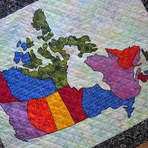 May include: A quilted fabric map of Canada with a white background and a black border. The map is divided into provinces and territories, each with a different patterned fabric. The provinces and territories are outlined in black.