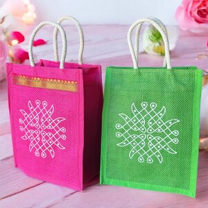 May include: Two small, reusable jute gift bags with white rope handles. The bag on the left is pink with a white design, and the bag on the right is green with a white design.