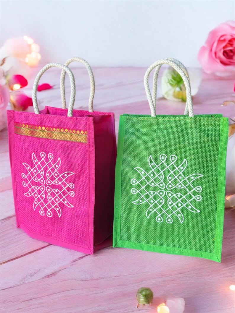 May include: Two small, reusable jute gift bags with white rope handles. The bag on the left is pink with a white design, and the bag on the right is green with a white design.