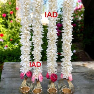 May include: Three white flower garlands with pink flowers at the bottom, each with a gold metal candle holder. The candle holders have a decorative wire design.