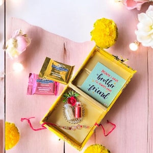 May include: A yellow wooden box with a decorative Rakhi bracelet, two small bottles, and a card that reads "Because I have a brother, I'll always have a friend." Also, two Ghirardelli chocolate squares.