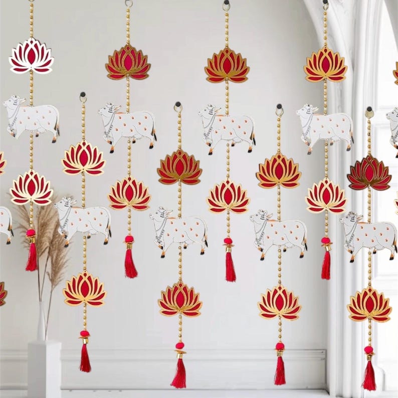 May include: A set of 12 decorative hanging ornaments featuring a white cow and a red and gold lotus flower. The ornaments are strung on a gold chain with a red tassel at the bottom.