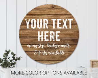 May include: A circular wooden sign with a horizontal plank texture. The text "YOUR TEXT HERE" is printed in a bold, distressed white font, followed by the white script text "many size, backgrounds, & fonts available" and "MORE COLOR OPTIONS AVAILABLE".