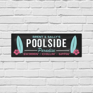 May include: A rectangular black sign featuring the text BRENT & SALLY'S POOLSIDE Paradise SWIMMIN' CHILLIN' SIPPIN' in white and light blue. The design includes two light blue surfboards and two pink hibiscus flowers on the left and right sides.