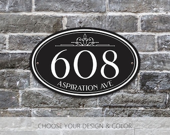May include: An oval black house address plaque featuring the white number 608 and the text Aspiration Ave in a serif font. The sign includes a decorative flourish above the number, a double-line border, and two small mounting holes on the sides.