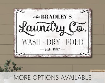 May include: A rectangular white sign with black text featuring the words the BRADLEY'S Laundry Co. in a decorative script font, followed by the words WASH · DRY · FOLD and Est. 1987, all enclosed within a thin black border with ornate corner details.