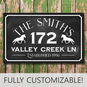May include: A rectangular black sign with white text and graphics. The sign features the text THE SMITH'S, the number 172, VALLEY CREEK LN, and ESTABLISHED 1996. Two white horse silhouettes flank the number 172. The sign has a white border.