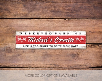 Peut inclure: Une plaque rectangulaire en métal avec un fond blanc et rouge portant le texte RESERVED PARKING, Michael's Corvette et LIFE IS TOO SHORT TO DRIVE SLOW CARS, ainsi que deux paires de drapeaux à damier croisés sur la bande centrale rouge.