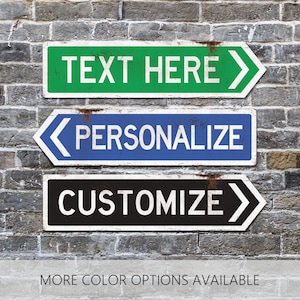 May include: Three arrow-shaped signs with the words "TEXT HERE", "PERSONALIZE", and "CUSTOMIZE" in white text. The signs are green, blue, and black, respectively, and are mounted on a brick wall. The bottom of the image reads "MORE COLOR OPTIONS AVAILABLE."