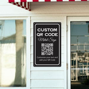 May include: A black metal sign with white text that reads "CUSTOM QR CODE Metal Sign." The sign includes a QR code and the text "Customize your text and add your QR Code." The sign is mounted on a white wall next to a glass door.