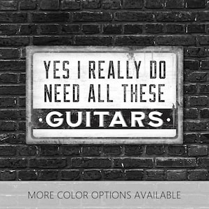 May include: A rectangular sign with the text "YES I REALLY DO NEED ALL THESE GUITARS" in a distressed font. The sign is mounted on a brick wall. The words "MORE COLOR OPTIONS AVAILABLE" are at the bottom.