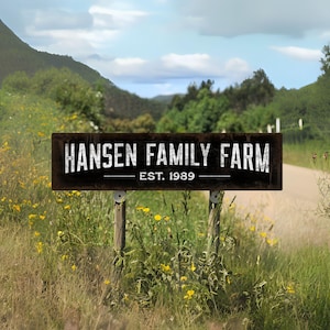 May include: A rectangular dark brown sign with a weathered texture featuring the white text HANSEN FAMILY FARM and EST. 1989. The sign is mounted on two wooden posts positioned in a field with yellow wildflowers and green grass under a blue sky.
