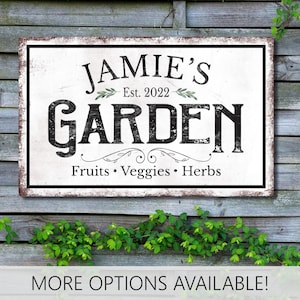May include: A rectangular white sign with a distressed black border and black text that reads JAMIE'S Est. 2022 GARDEN Fruits • Veggies • Herbs. The sign features small green leaf illustrations flanking the text Est. 2022 and decorative flourishes.