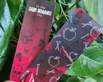 May include: Two bookmarks with a dark romance theme. One bookmark is red with skulls and roses and the text "In my DARK ROMANCE Era". The other bookmark is black with white apples and nails.