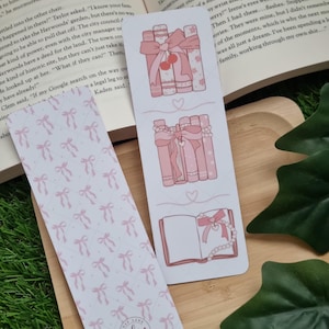 May include: Two pink and white bookmark designs. The first bookmark features a stack of pink books with a pink bow and cherries. The second bookmark features a pink open book with a pink bow and a string of pearls. Both bookmarks have a pink and white bow pattern.