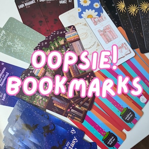 May include: A collection of rectangular paper bookmarks featuring various designs including dark red with skull patterns, blue with white daisies, black with gold suns, blue with dragon silhouettes, and colourful stripes with small green cauldron illustrations.