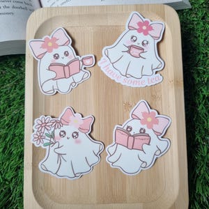 May include: Four cute ghost stickers with pink bows and flowers. The ghosts are holding a book, a cup of tea, a bouquet of flowers, and a book. The text "I have some tea" is written below one of the ghosts.