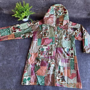 Pode incluir: Uma jaqueta com capuz patchwork em uma variedade de cores, incluindo vermelho, verde e marrom. A jaqueta apresenta uma frente abotoada e mangas compridas. O design incorpora vários padrões e formas.