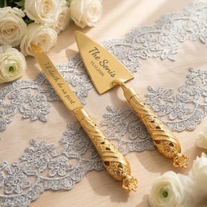 May include: A gold-toned cake knife and server set with ornate, textured handles. The knife blade is engraved with the text 'Til death do us part', while the triangular server blade features the engraved text 'The Sonis' and '05.01.2026'.