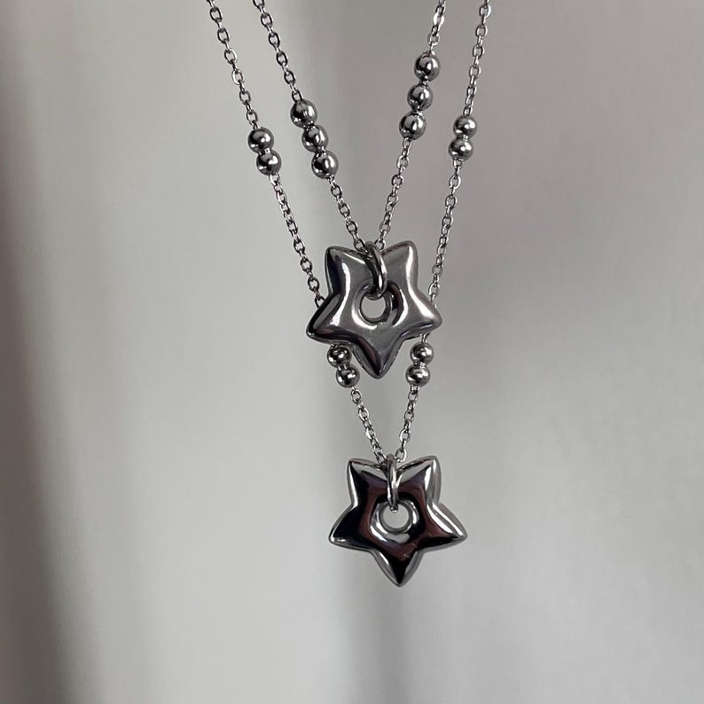 Peut inclure: Un collier en argent avec deux pendentifs en forme d'&eacute;toile. Les &eacute;toiles ont un trou au centre et sont reli&eacute;es &agrave; la cha&icirc;ne par un petit anneau.