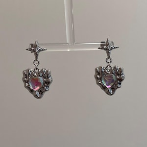 May include: A pair of silver earrings with a star charm and a heart-shaped iridescent stone.
