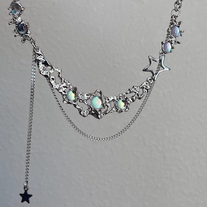 May include: A silver necklace with a crescent moon design, featuring iridescent stones and star charms. The necklace has a delicate chain with a dangling star charm.