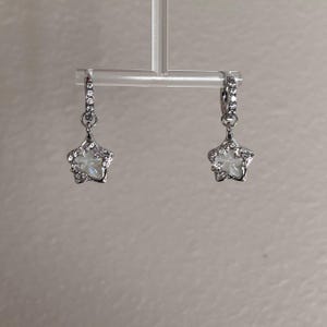 May include: A pair of silver star-shaped earrings with clear crystals. The earrings are hanging from a silver hoop.